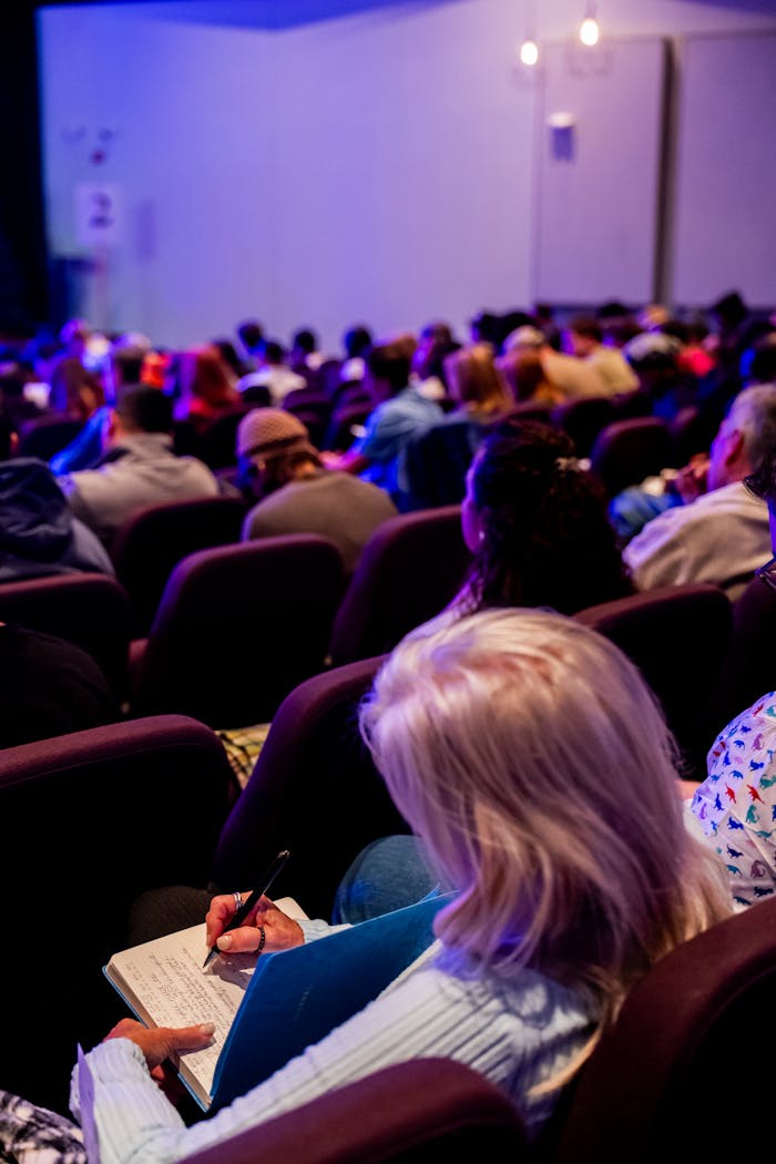 A diverse group of adults attending a conference, taking notes in an auditorium.