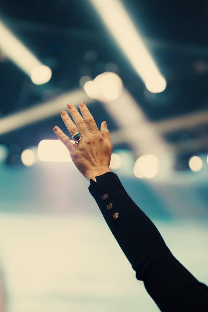 A solitary hand reaches up in a well-lit room, possibly symbolizing connection or participation.